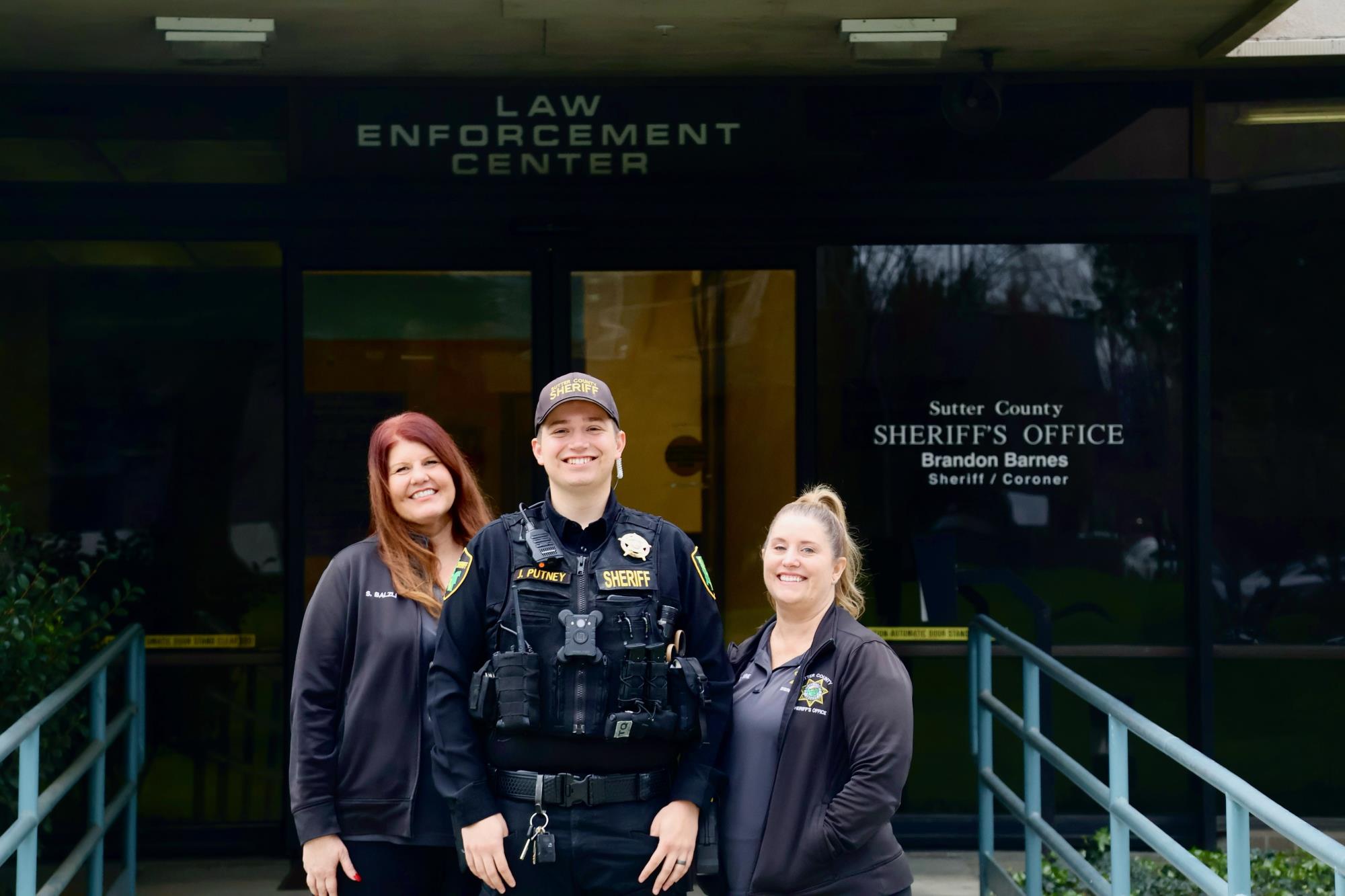 Suzanne, Deputy Putney and Kathi posing for a photo in front of the Sheriff's Office Building